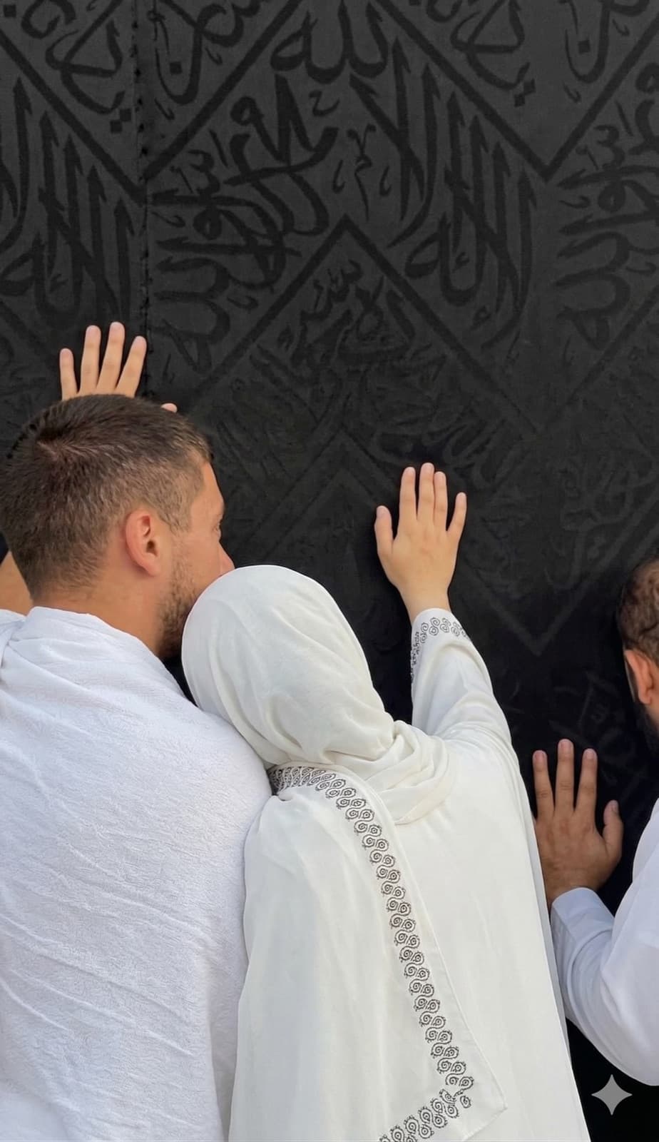 A couple reaching out to touch the Kaaba's kiswah together in Makkah